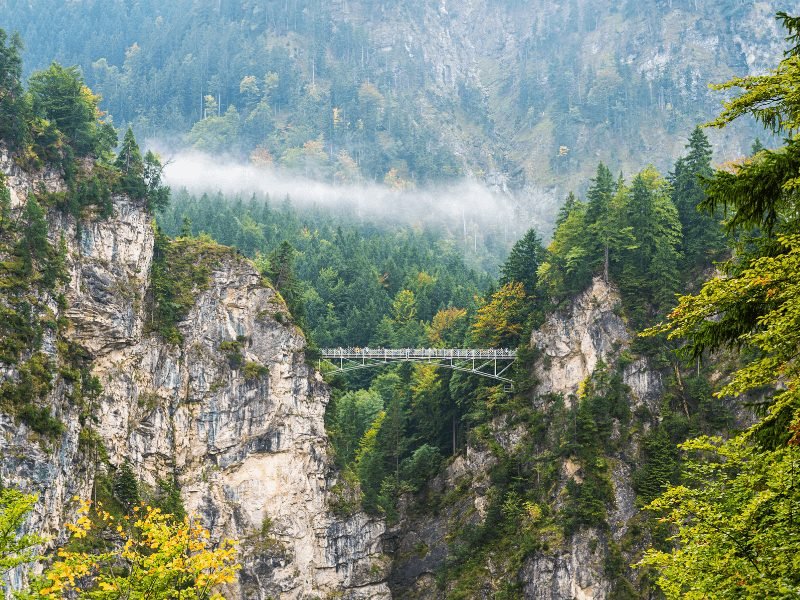 The Marienbrucke near Neuschwanstein Castle near Fussen Germany, a small bridge with green foliage around it and a misty landscape