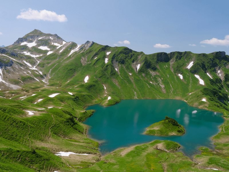 alpine lake in the alps, called schreksee, with green mountain, teal water, and snowy patches on the mountain crevices