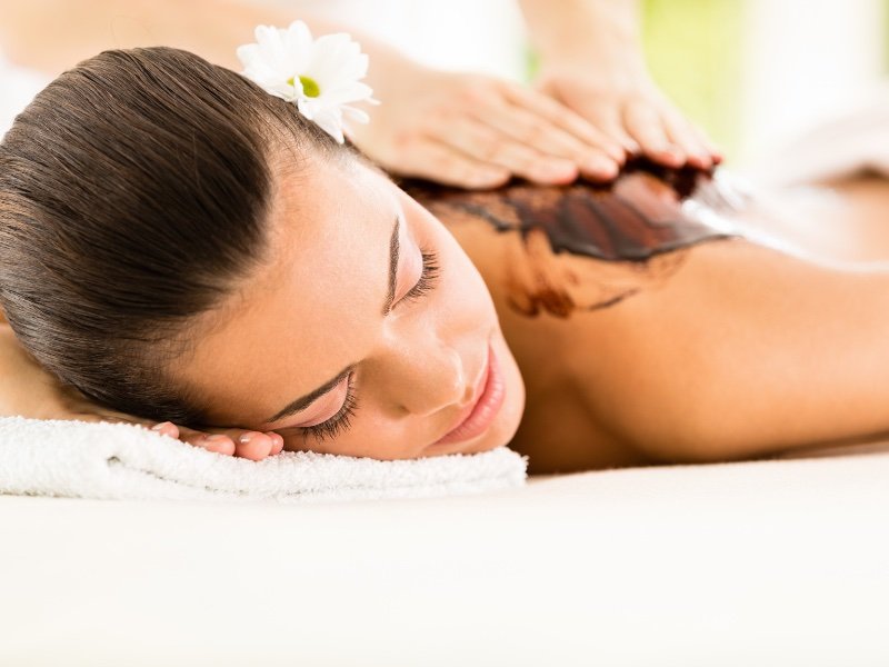 woman receiving a chocolate massage with a flower in her hair, looking relaxed