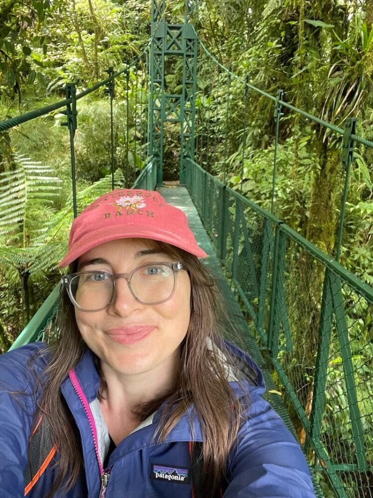 allison green wearing a jacket and hat smiling in the forest walking around the hanging bridges of selvatura adventure park in monteverde canopy