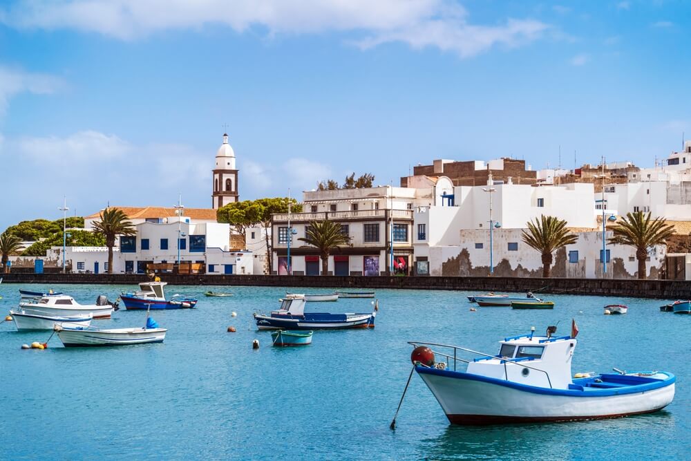 Beautiful quay with historic architecture and boats on blue water in Arrecife, Lanzarote, on a sunny day with just a few clouds in the sky and a spectacular view of the white-washed old town landscape