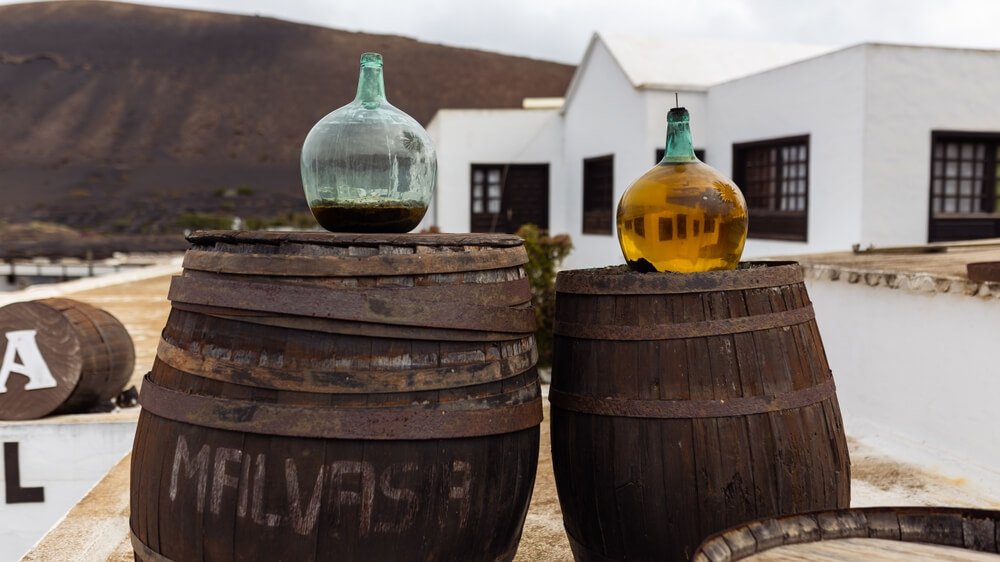 Glass bottles with white volcanic wine - malvasia, standing on vintage wooden barrels against the backdrop of the winery, Lanzarote, Canary Islands, Spain
