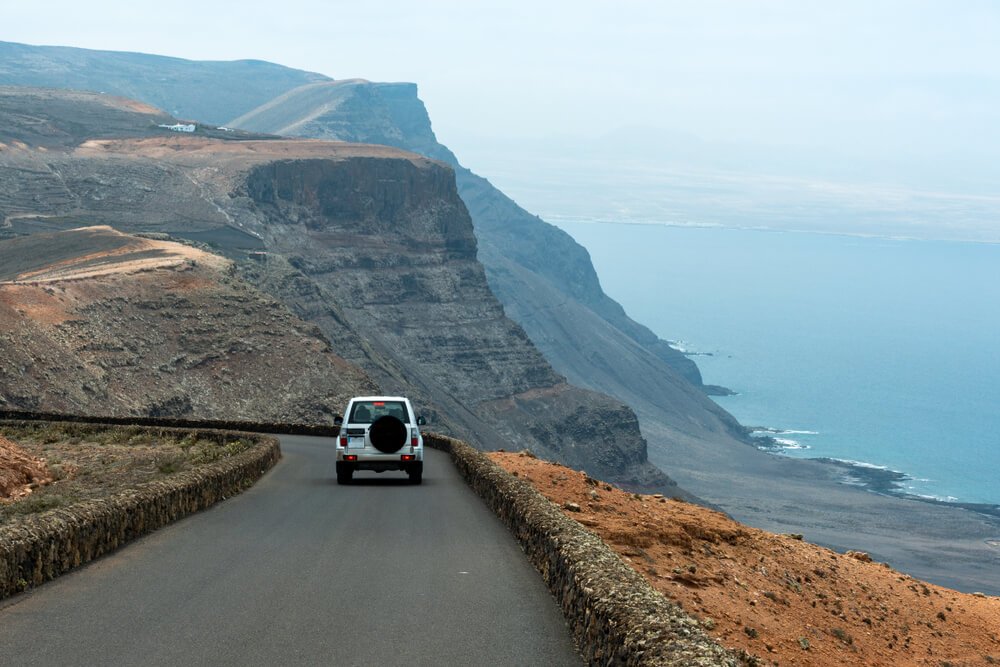 a car on a road in lanzarote driving off into the distance towards a viewpoint in the background