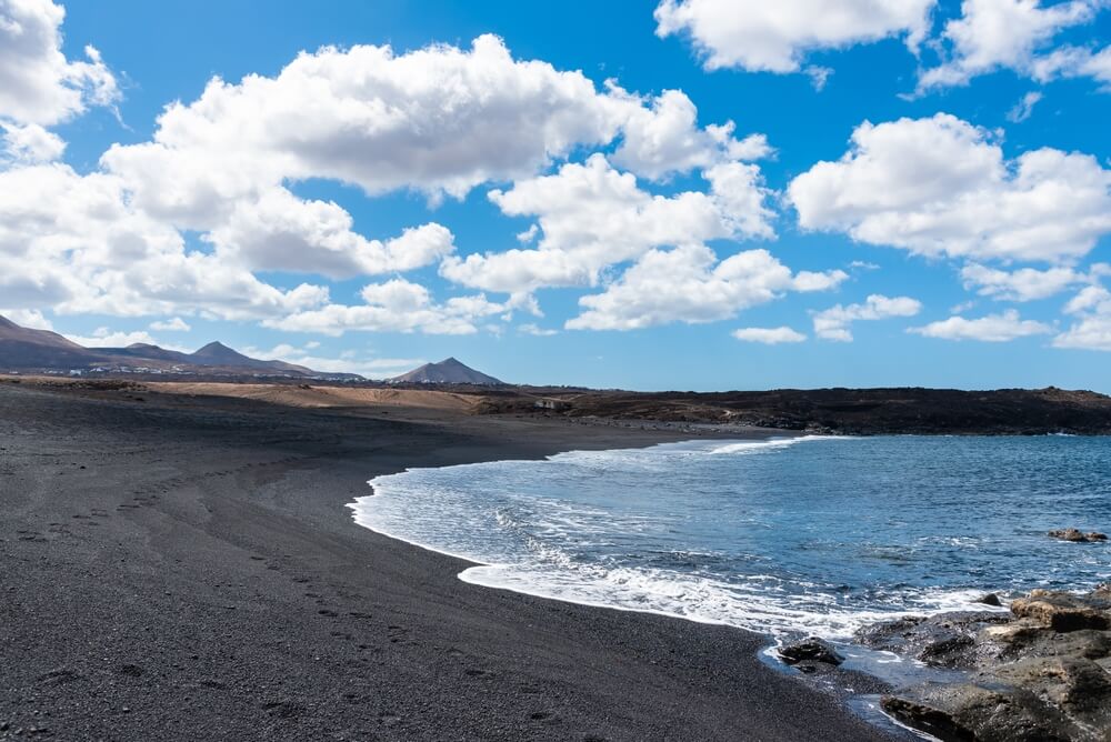 playa janubio, a black sand beach in lanzarote wtih blue ocean next to black volcanic sands