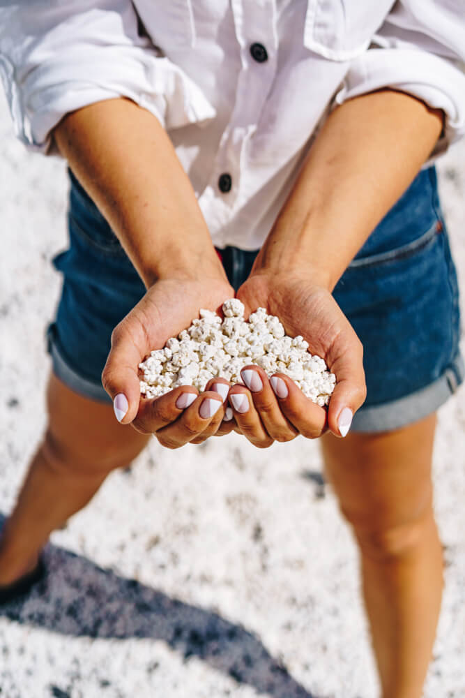 Woman is holding handful of white coral stone looking like popcorns. Popcorn beach near Corralejo in Fuerteventura island.