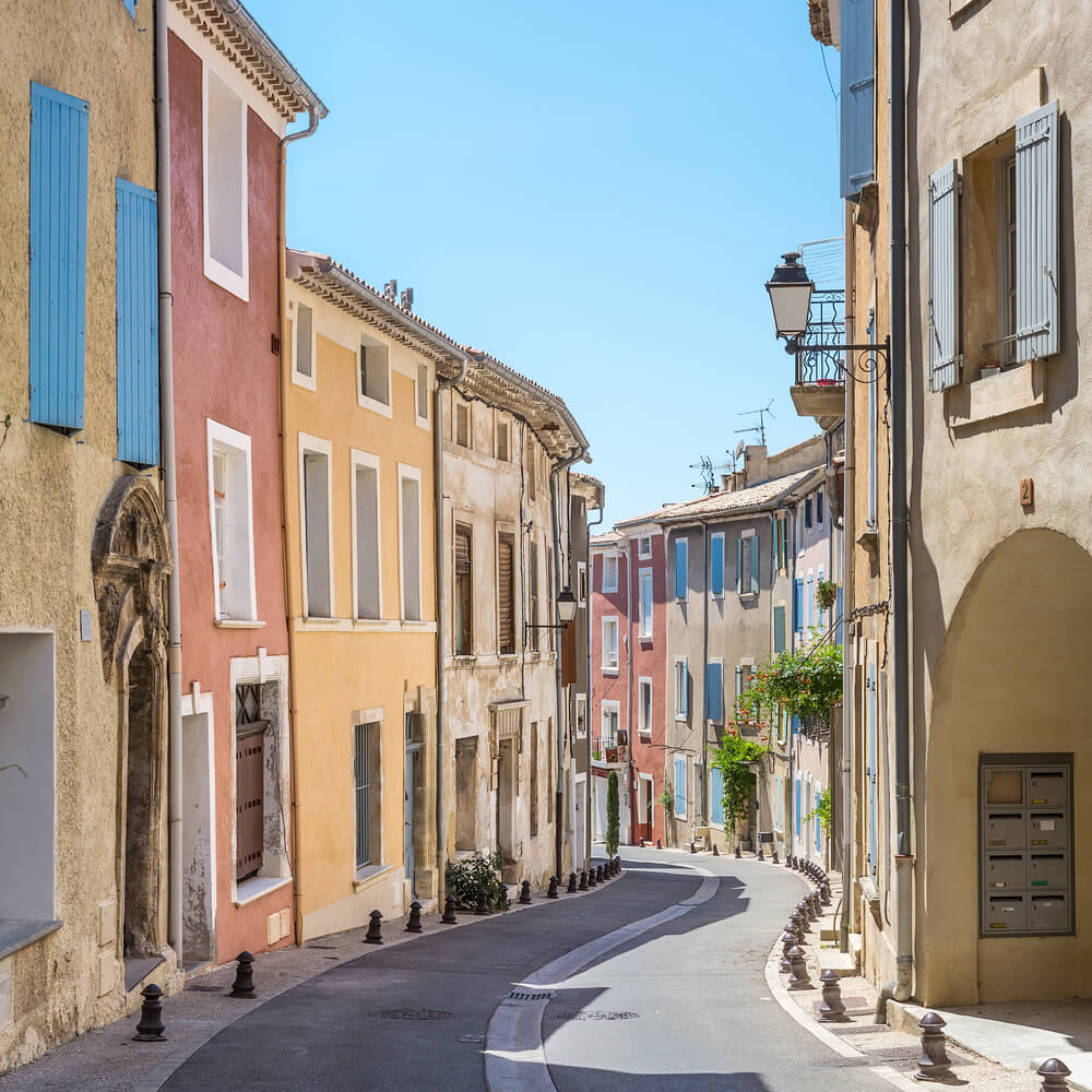 Typical houses in a narrow street in city center of Saint-Saturnin-les-Apt, a small village in French Provence. Pastel colors of red, yellow, beige with blue window shutters on some of the buildings.