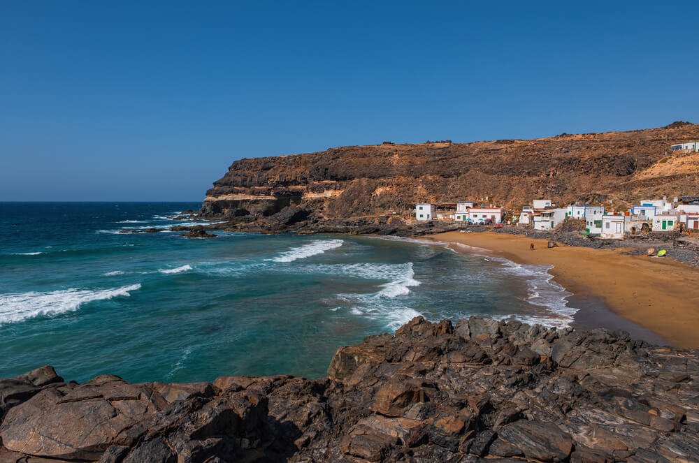 Playa Puertito de Los Molinos with darkish orange brown sand and white washed houses on the shore