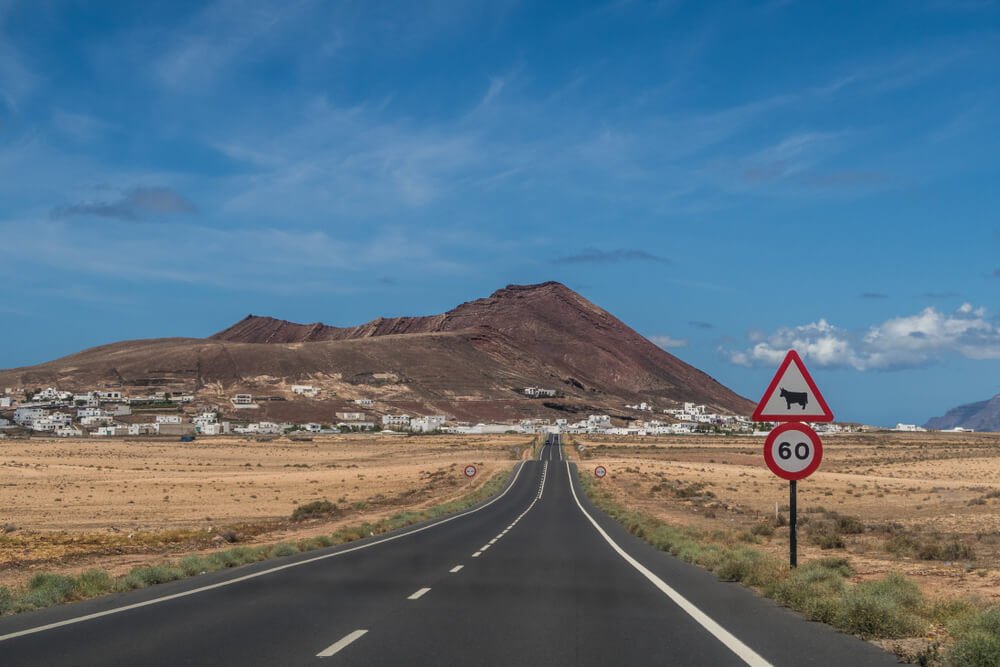 Empty road in Lanzarote sign about cow crossing and 60 kilometer per hour speed limit with volcano in background