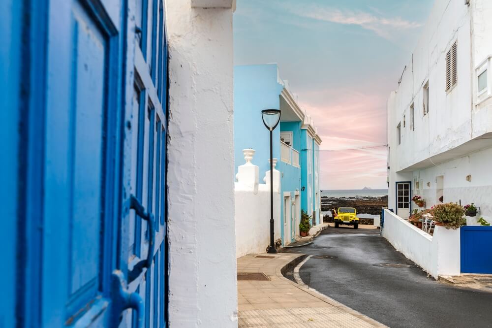 Yellow 4-wheel drive car on narrow street with white and blue buildings in Corralejo, Lanzarote, Canary Islands, Spain