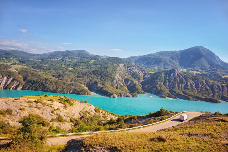 a car on the road with a beautiful lake in the background in provence