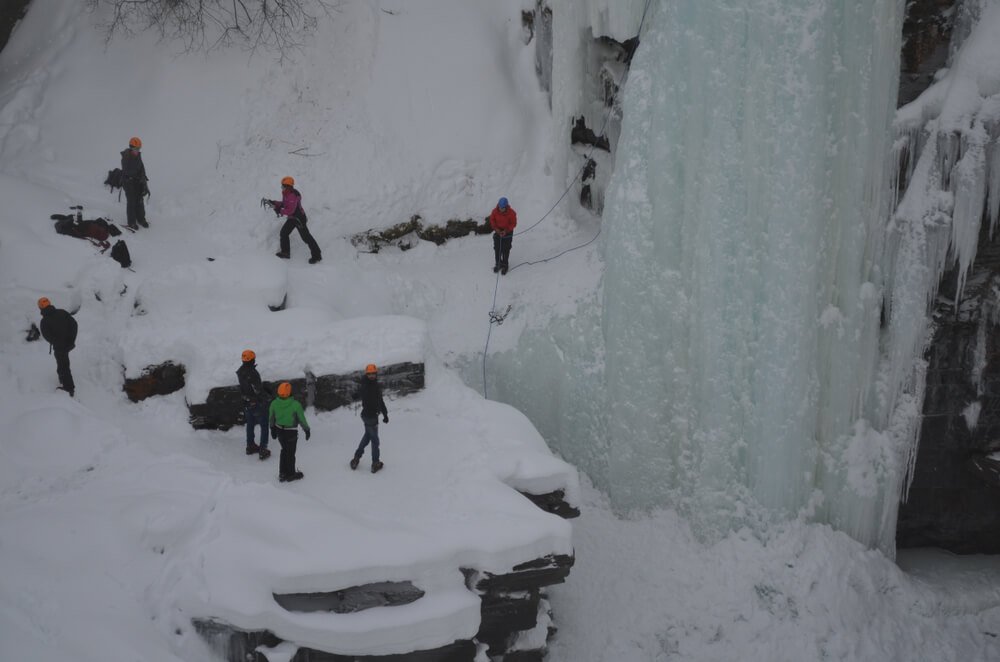 people doing ice climbing in abisko national park, sweden with lots of of cold weather gear, helmets, and visible frozen waterfall