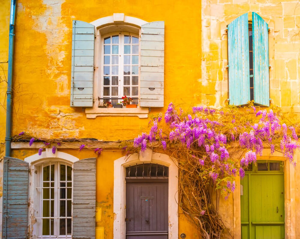 bright yellow house with shutters in blue and purple blooming flowers.