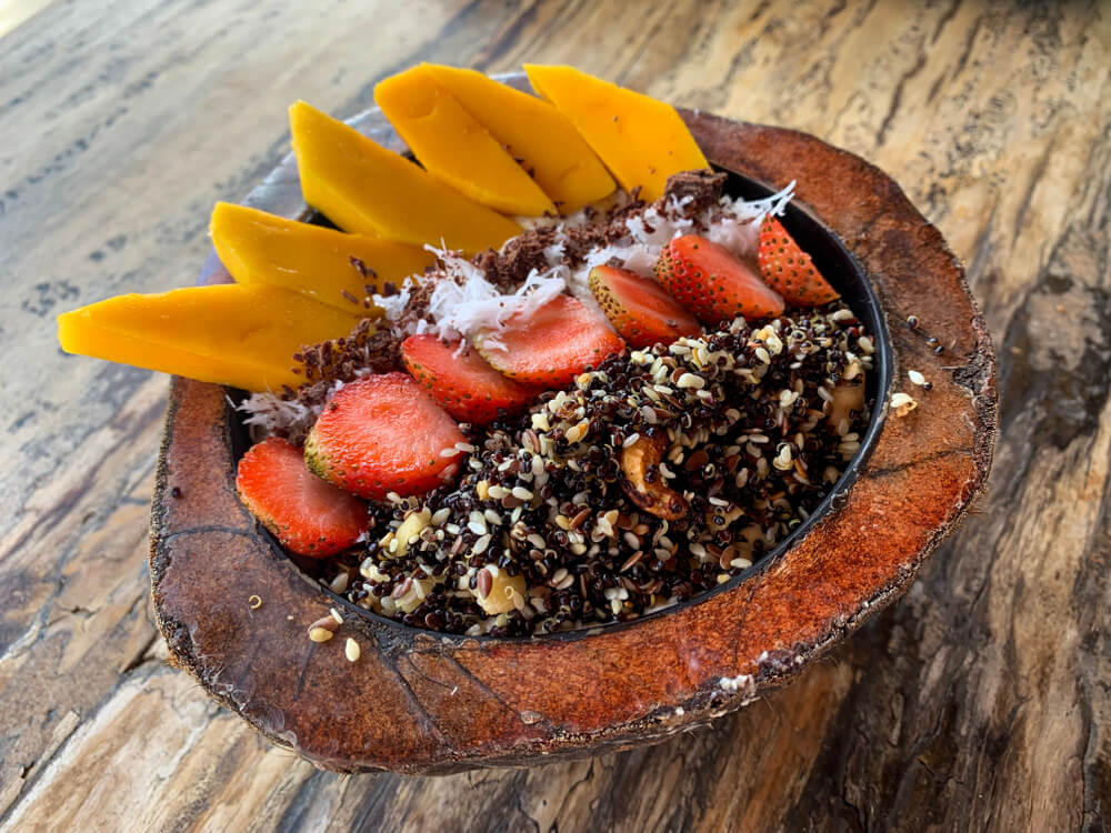 Smoothie bowl served inside of a coconut bowl with mango and strawberry and seeds and coconut shreds in Bali