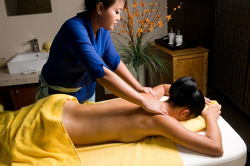 woman receiving a back massage at a bali spa with flowers in the background