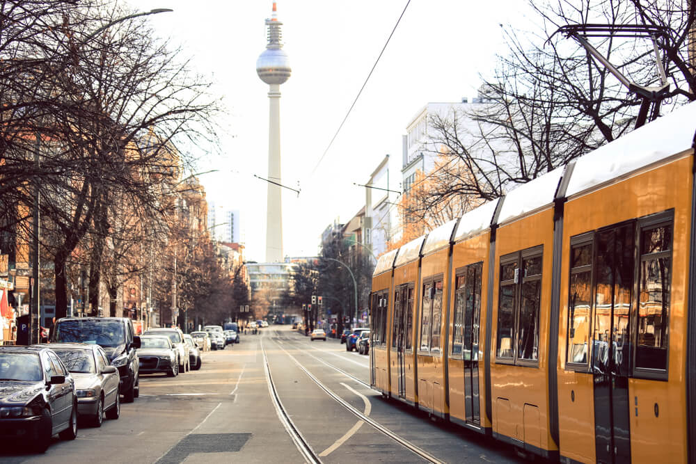 Yellow public streem car tram passing by the streets of Berlin, with the landmark of Berlin, the famous TV tower, towering over the city skyline.
