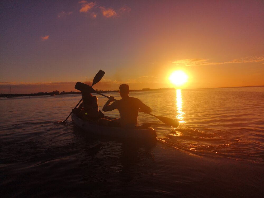 two people in a double kayak with the sun sinking down at sunset on the island