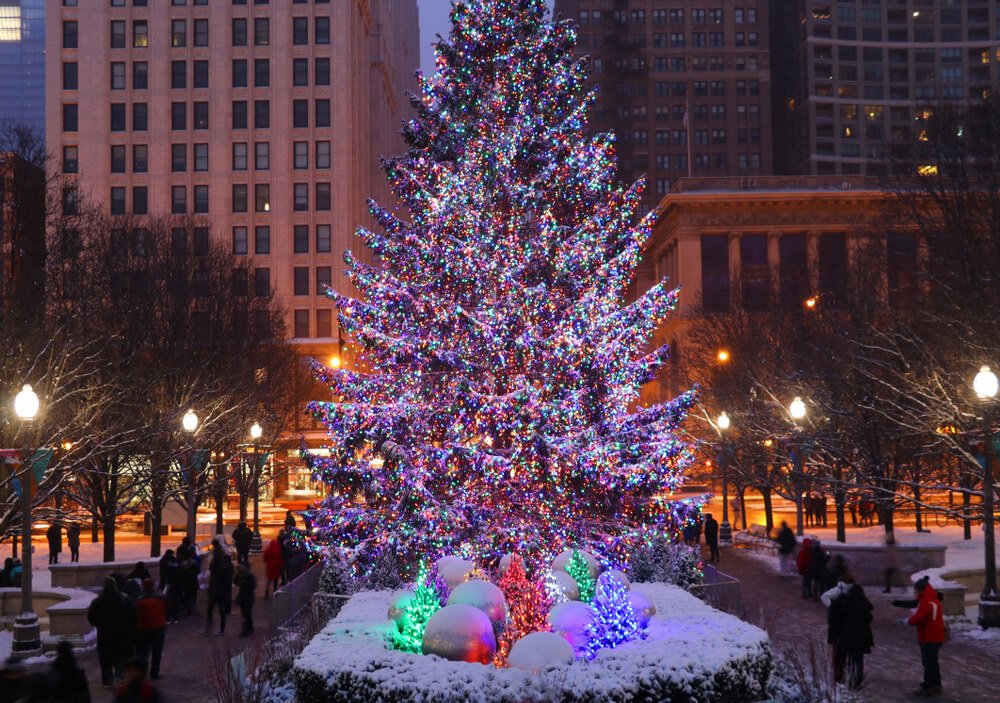 big lit up christmas tree in the city of chicago with baubles underneath and people walking around