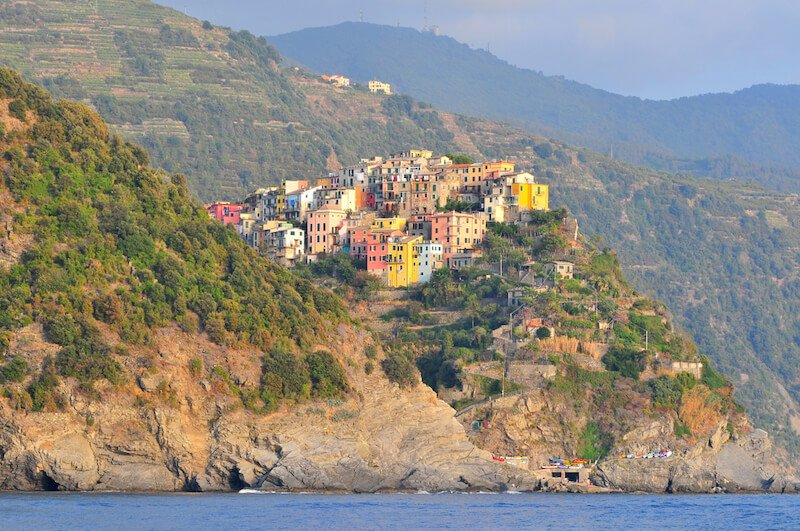 The town of Corniglia in the Cinque Terre, with its multi colored buildings among hills and a rocky coastline view
