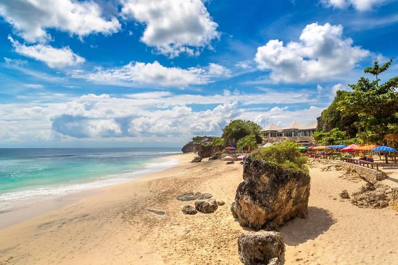 The beautiful white sands and blue waters of the idyllic Dreamland Beach on Bali in a sunny day with some patchy clouds in the sky. Not too many people on the beach.
