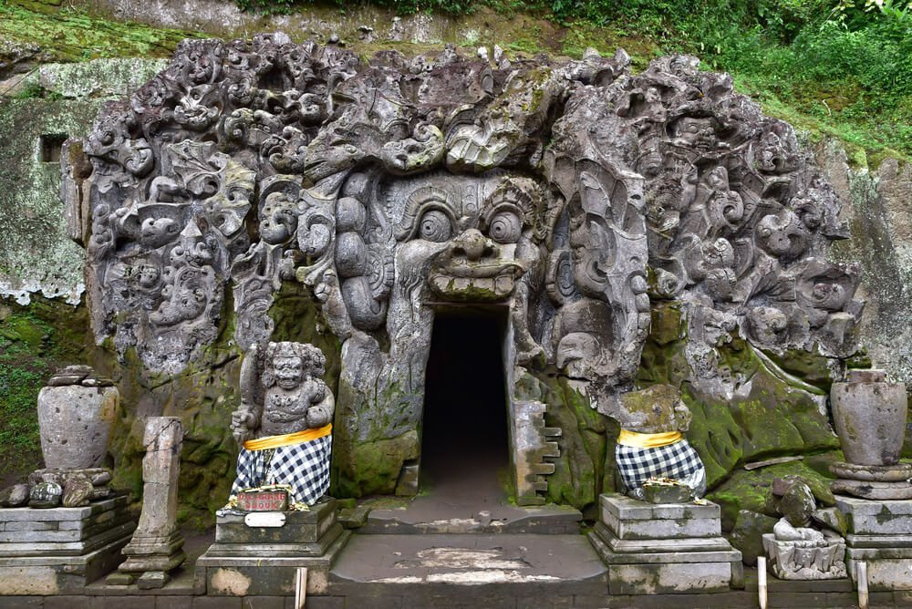stone face carved into a cave entryway, guarded by two figures, at the goa gajah temple in bali, indonesia not far from ubud and its waterfalls