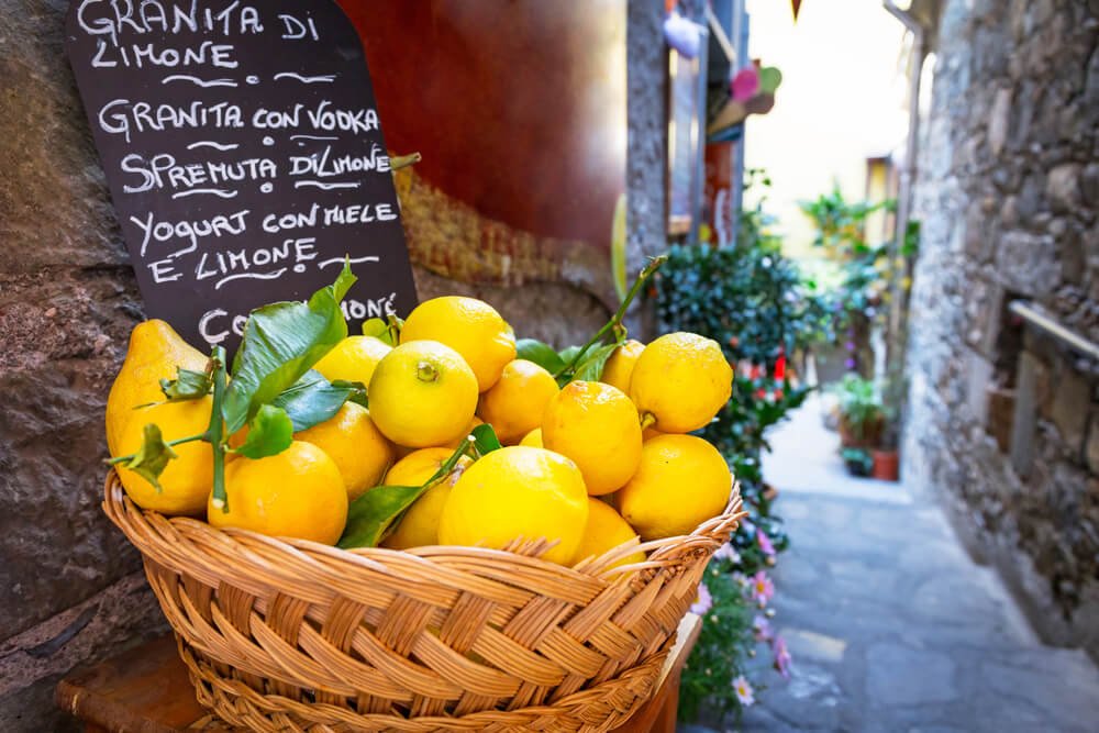 A handwritten chalkboard with various Italian dessert offers and a basket full of lemons in Corniglia village of the Cinque Terre