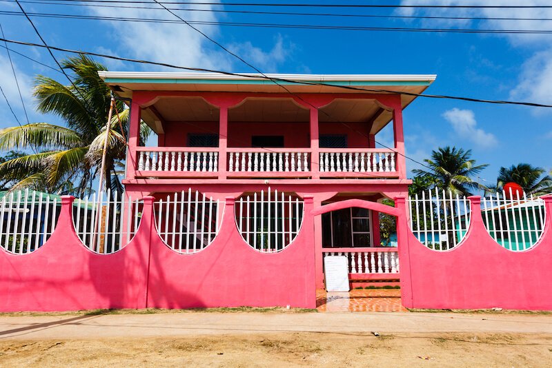 bright pink facade of 2 story house on a dirt road on little corn island