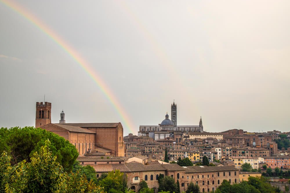 View of the famous cathedral of Siena (Duomo) as seen from the Medici Fortress with a rainbow over the city