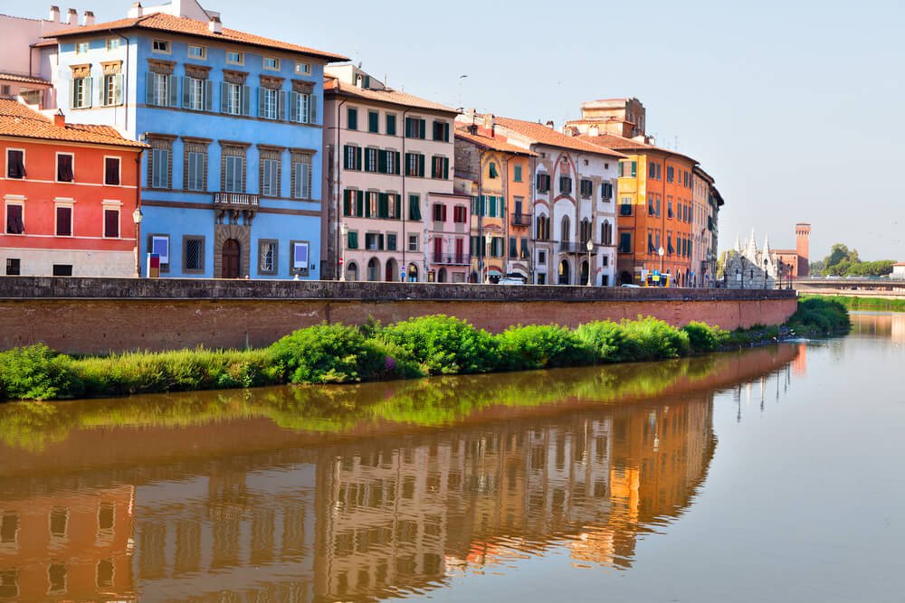 Blue building of Palazzo Blu with other buildings along the Arno waterfront in Pisa, with reflection on a sunny day