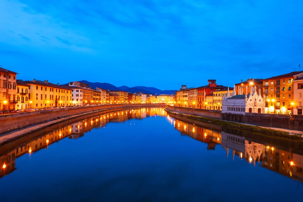 Night view of the lit up colorful houses along the Arno river waterfront in Pisa's city center