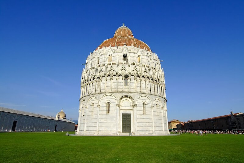 The Baptistry of St. John, Pisa, a round building with white marble and a red tile roof, with lots of tourists around