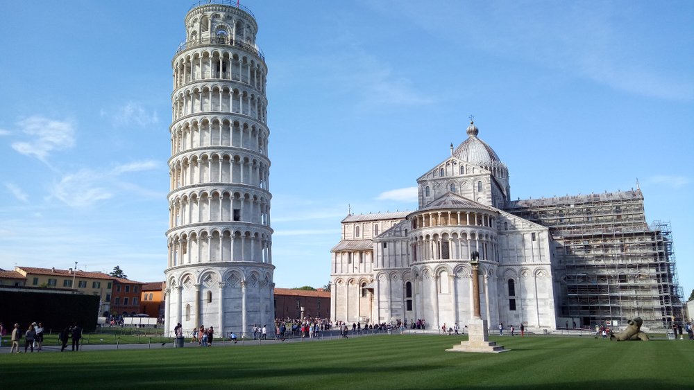 The structure of the Duomo cathedral of pisa and the famous leaning tower of pisa, with lots of tourists around, on a clear sky day