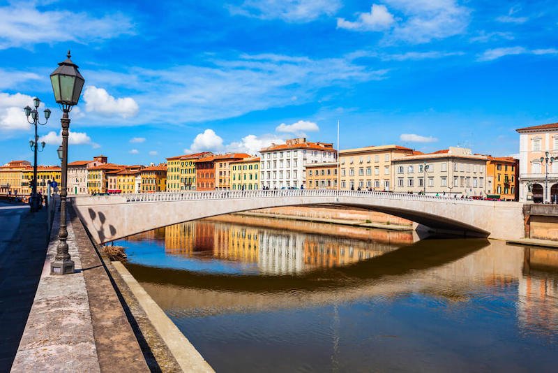 The Arno River with the Ponte Solferino bridge spanning across it, framing colorful houses of the Arno Waterfront.