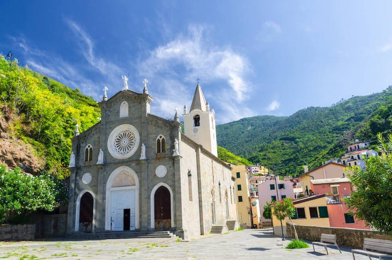 San Giovanni Battista catholic church in the valley of Riomaggiore traditional typical Italian village in National park Cinque Terre, green hill, blue sky, in the green hills of the surrounding countryside
