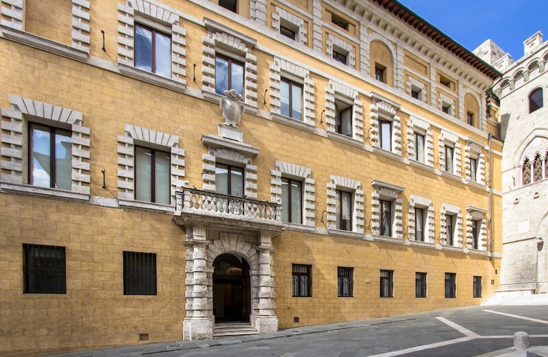 Yellow facade of the building called Palazzo Spannocchi which is part of Piazza Salimbeni in the Siena historical center, a must visit on a Siena itinerary
