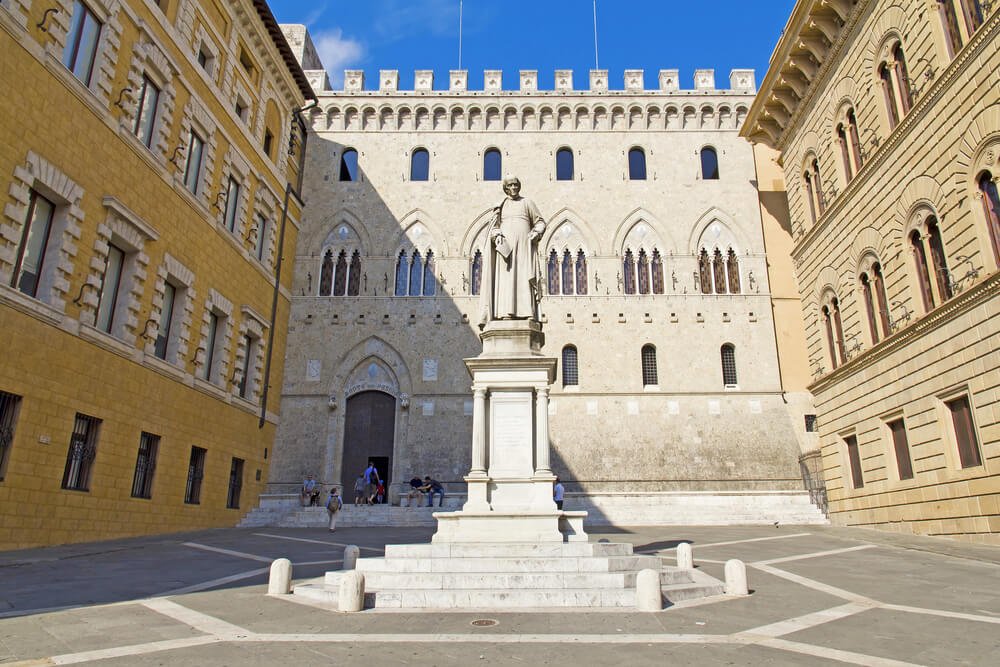 Monument to Sallustio Bandini and yellow-hued building of Palazzo Spannocchi in the famous Piazza Salimbeni, part of Siena key landmarks.
