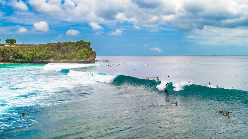 a beach in uluwatu bali with surfers enjoying the waves on a sunny day