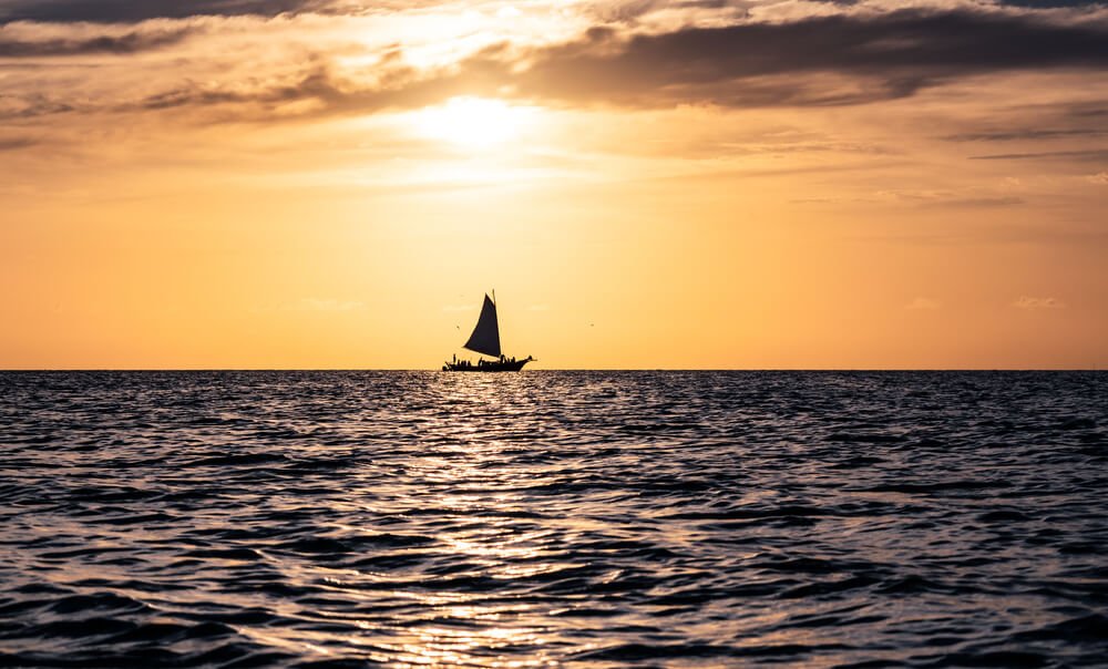 sunset on the sea in belize with a ship with lots of people on it as the sun is going down