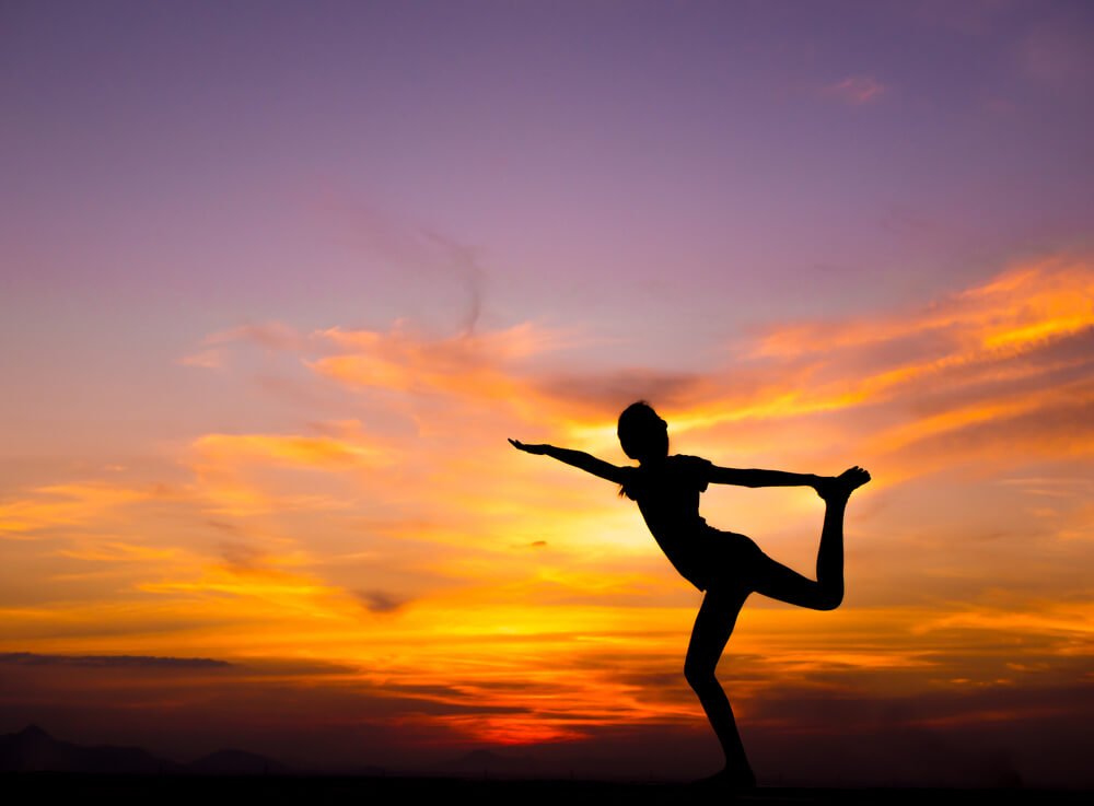 a dark black silhouette of a woman against a sunset sky doing yoga on a rooftop