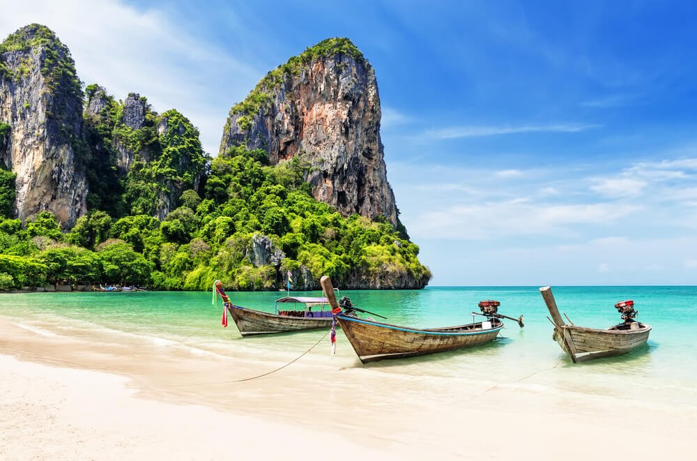 three famous thai longtail boats with the cliffside rock formations against the striking blue water