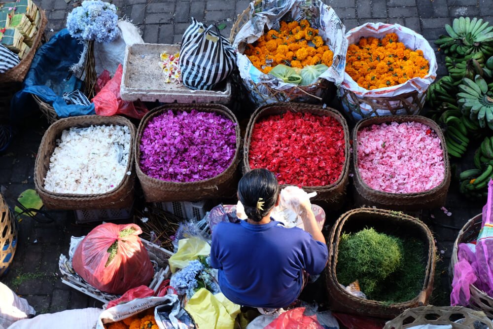 Ubud Market with a woman preparing the island's trademark offerings with orange, pink, purple, white flowers and rice