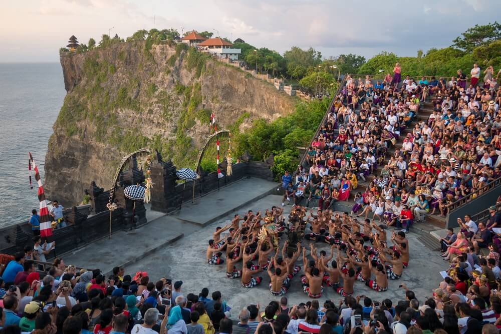 A group of tourists watching a show at the stunning cliffside Uluwatu Temple where locals perform the traditional Kecak Fire Dance in Uluwatu, Bali -- a must on any Uluwatu itinerary!