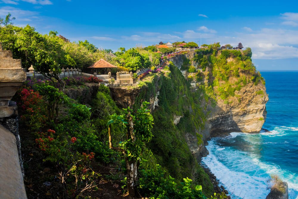 the view of uluwatu temple during the daytime on the cliffside with beautiful beach below it, characteristic of the uluwatu landscape you'll see on this uluwatu itinerary.