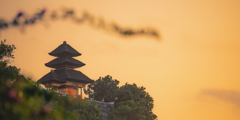 orange sky and uluwatu temple framed against the setting sun with some clouds remaining in the pastel orange sky