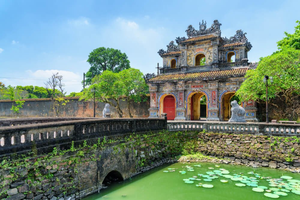 fancy gate to an imperial city in vietnam with a bridge with green water and lily pads in the water