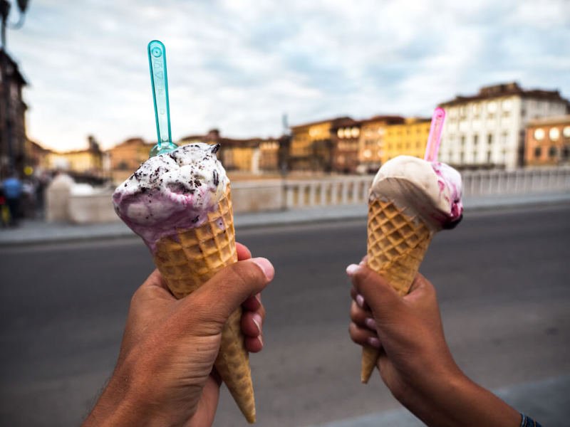 A man and a woman holding up two scoops of gelato with a backdrop of the Arno River in Pisa Italy
