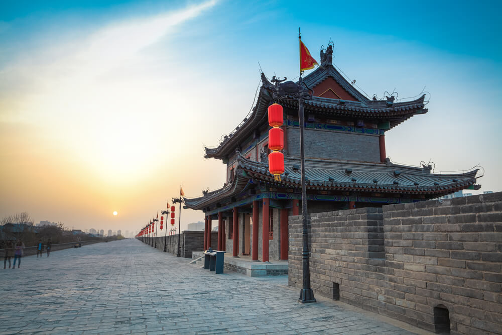 view of the skyline in xian with old city walls and an ancient tower on the wall, red lanterns, around sunset