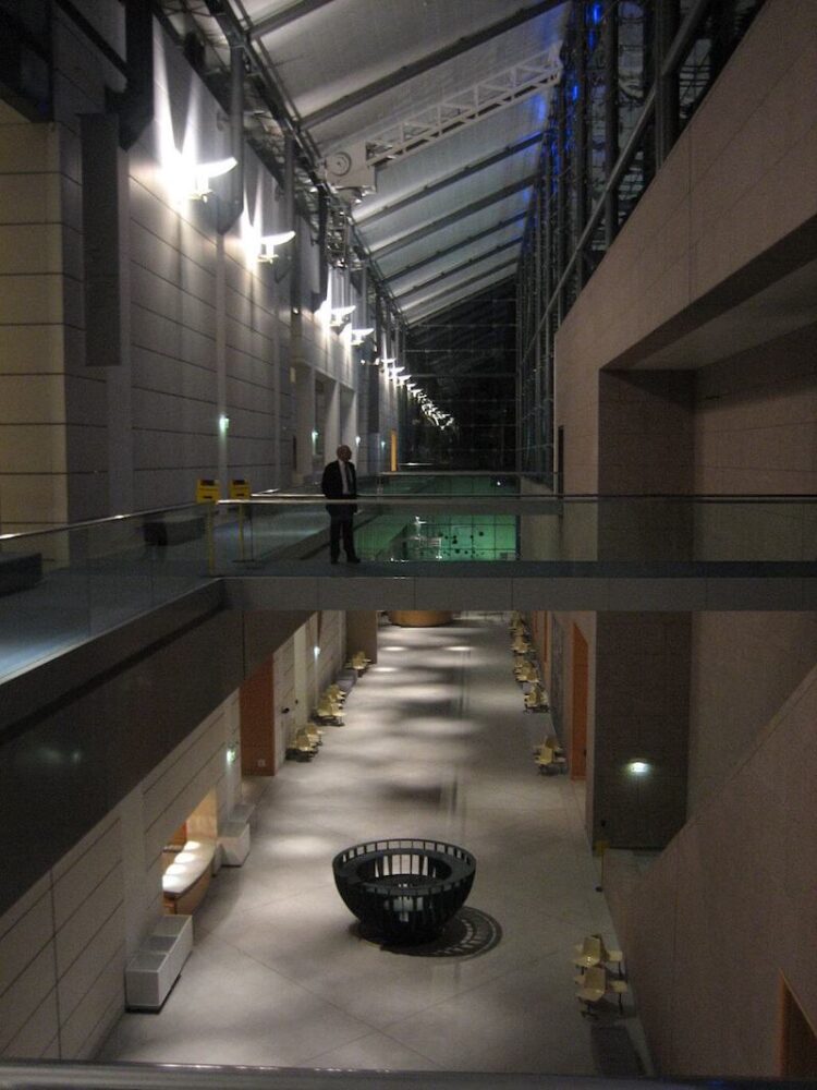 A man standing in a museum with the lights on while it is dark outside