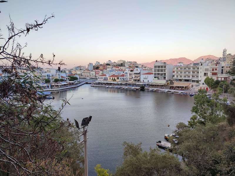 Sunset falling on the quaint port town of Agios Nicolos in the winter in Crete, when the island is very peaceful in January as a warm winter Europe getaway. Boats, houses, and mountains in the distance.