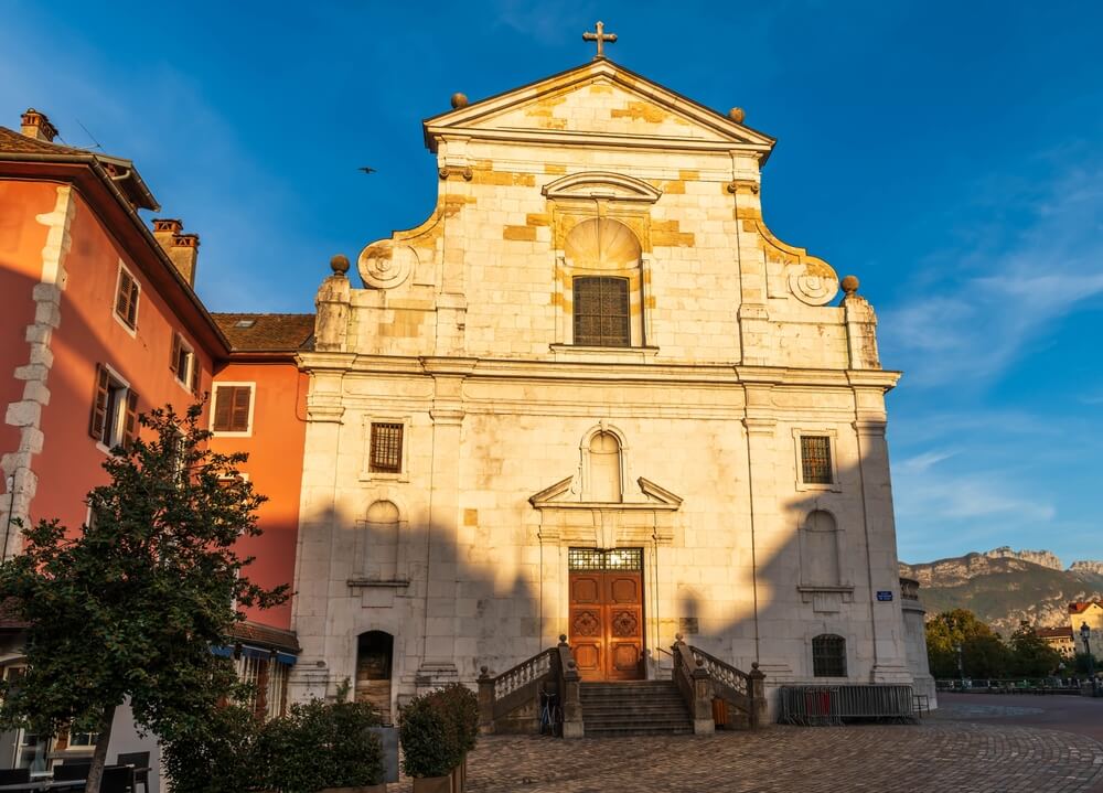 Church constructed primarily from what appears to be limestone or a similar pale stone, which gives it a warm and inviting glow, especially as it's kissed by the golden rays of the setting or rising sun. The façade is symmetrical and features a mix of classical architectural elements.