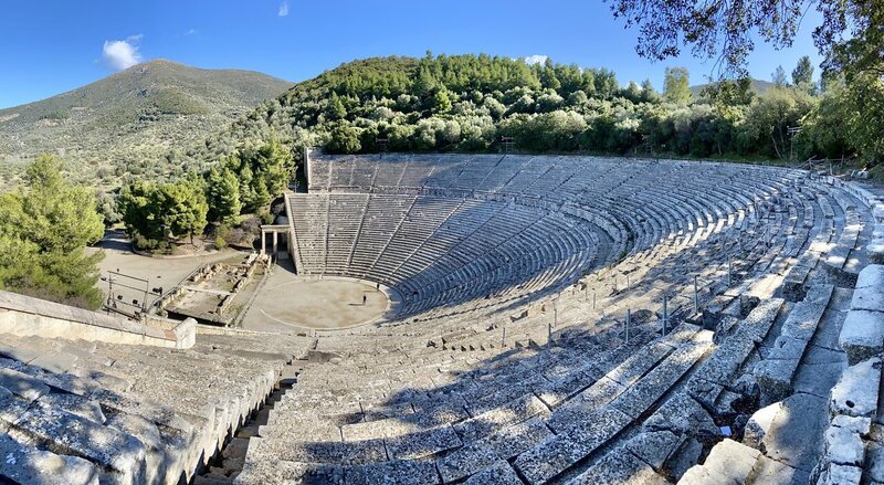 Nearly empty archeaological site in the Peloponnese peninsula of Greece with an amphitheater with no one inside it on a sunny day